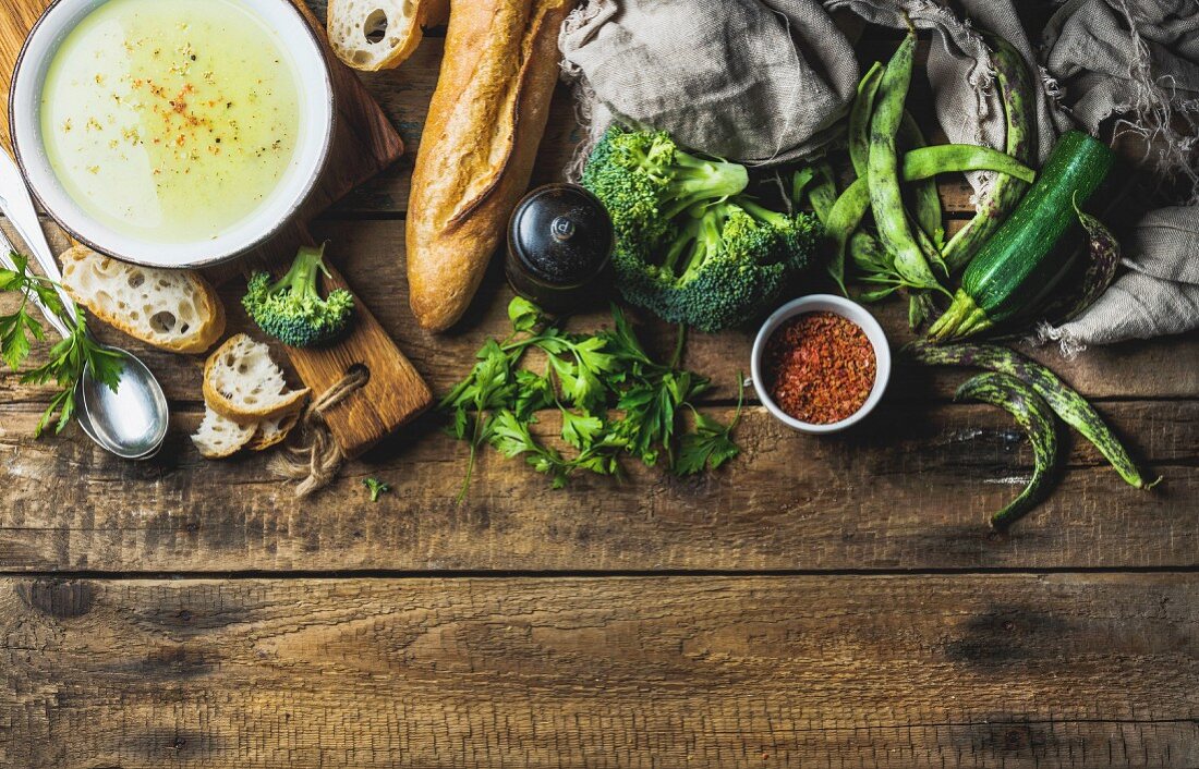 Gemüsecremesuppe mit Zucchini, Brokkoli und grünen Bohnen, Gewürze und Baguette auf Holzuntergrund