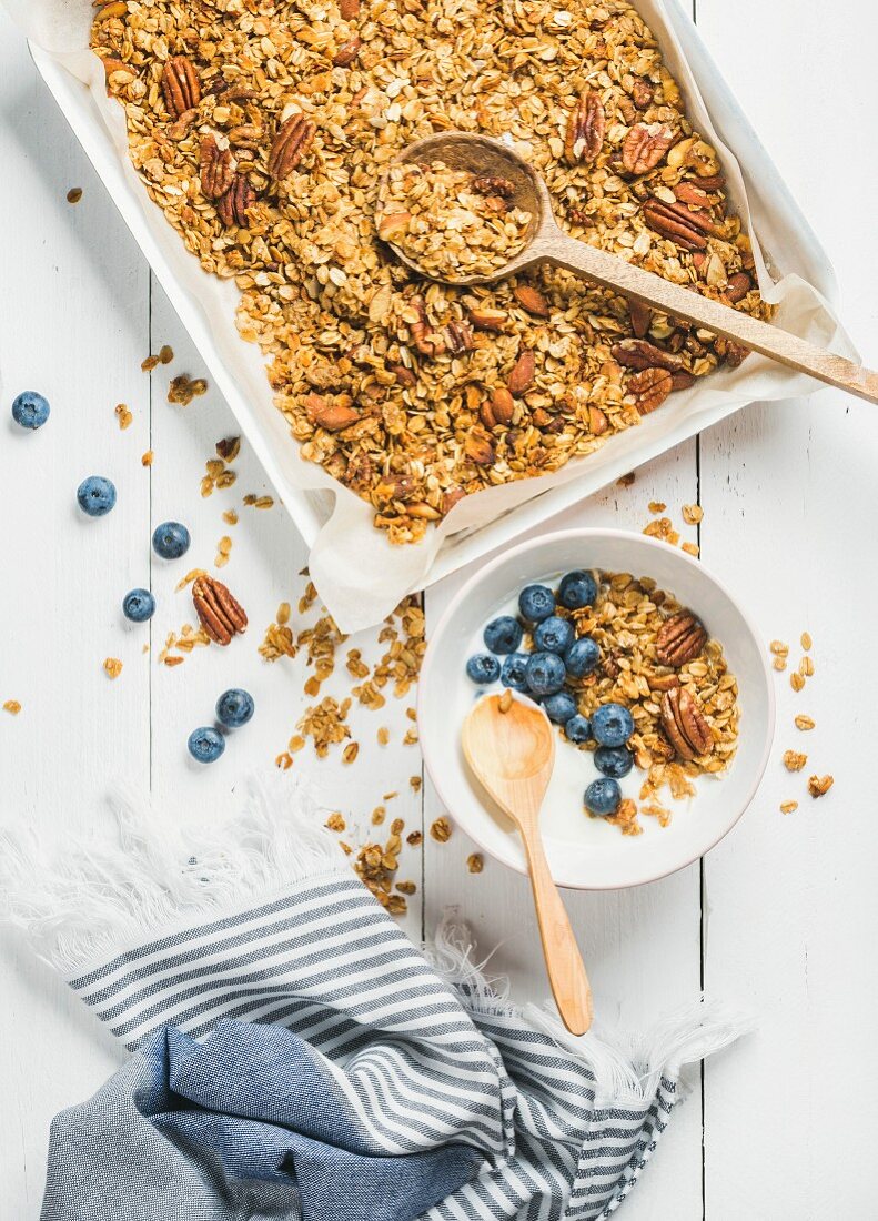 Hafermüsli mit Pecannüssen, Heidelbeeren und Joghurt in einer Schale auf weißem Holzuntergrund