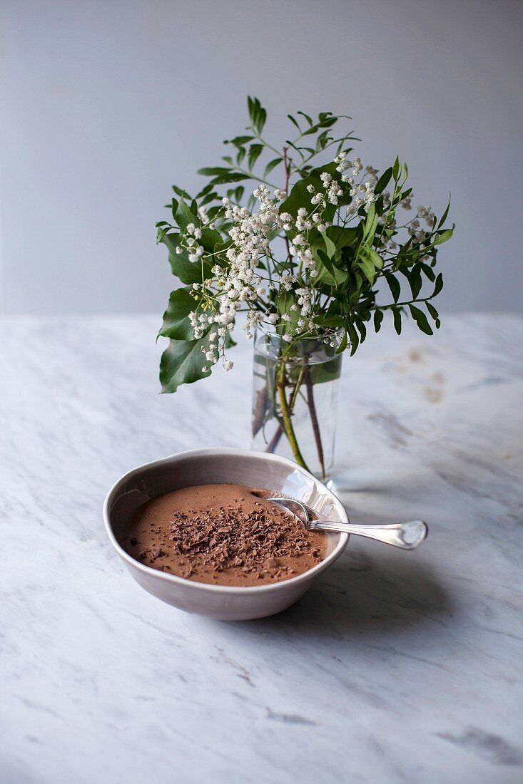 Chocolate mousse sprinkled with grated dark chocolate in a small bowl on a white marble table