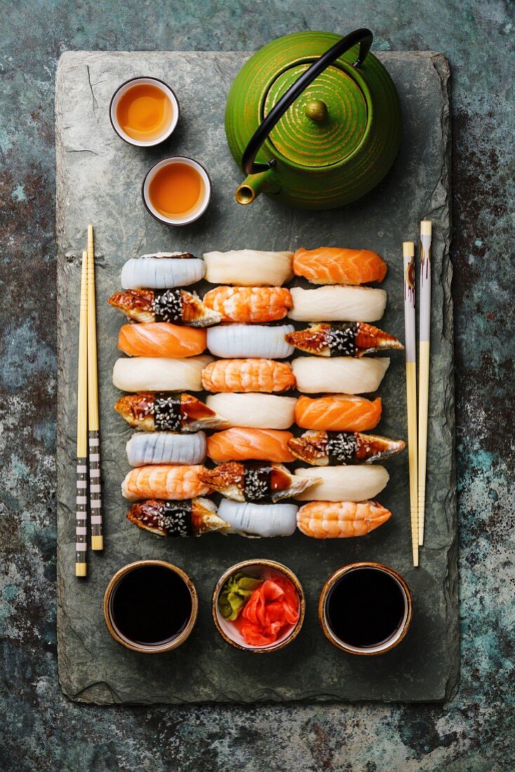 Nigiri-Sushi mit Essstäbchen für Zwei auf Schieferplatte und grüner Tee