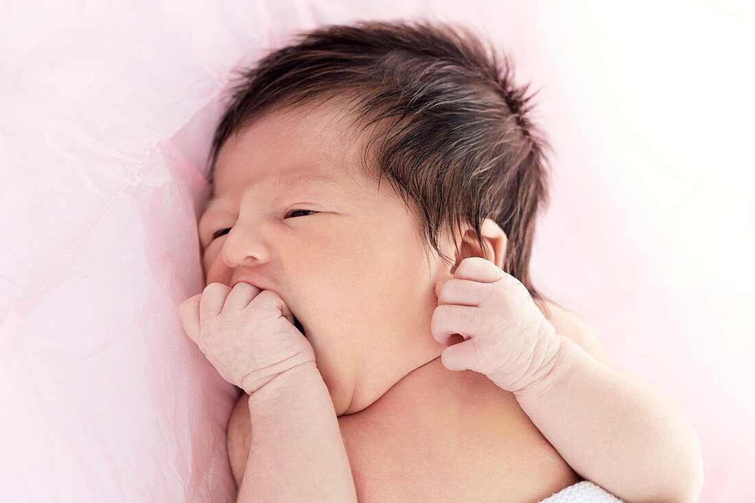 Newborn baby girl with hand in mouth