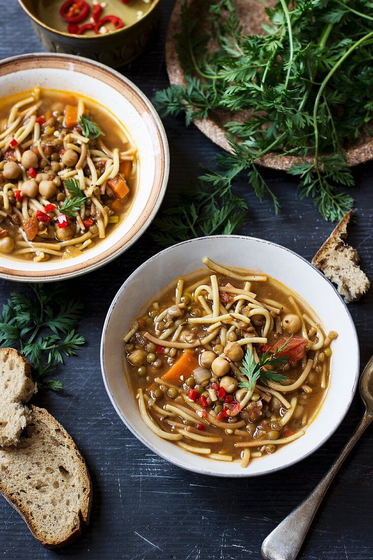 Noodle soup with tomatoes, chickpea and lentils servced with bread and carrot greens