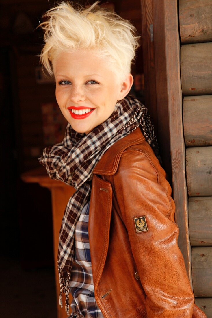 A blonde woman wearing a checked blouse, scarf and brown leather jacket