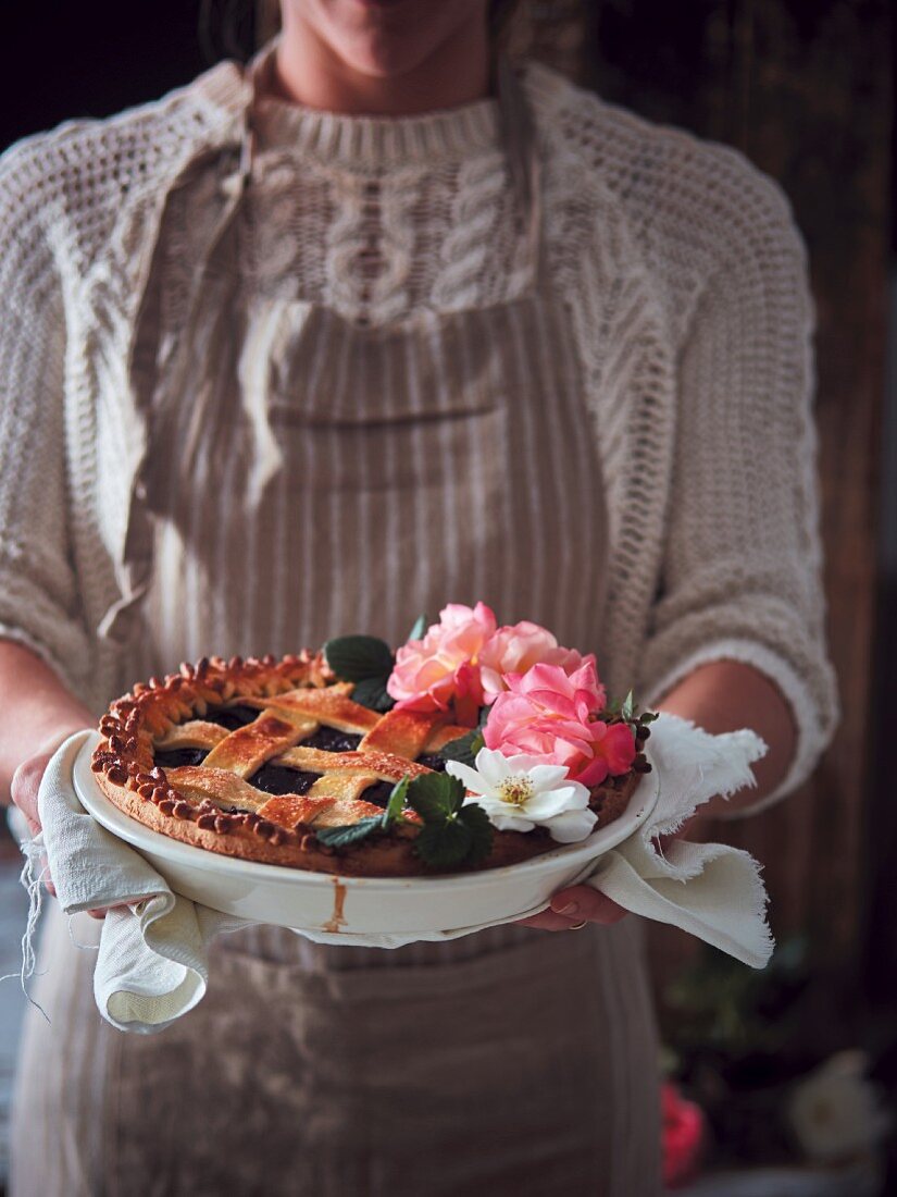 A woman holding a fruit pie with a lattice top and rose flowers