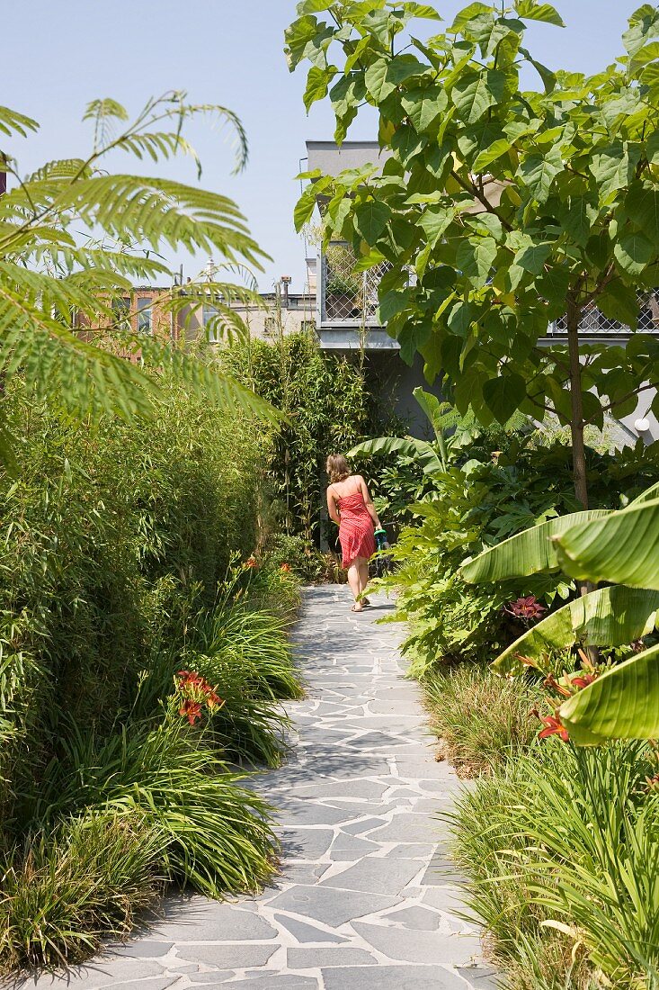 Woman walking along stone-flagged path leading through summery garden