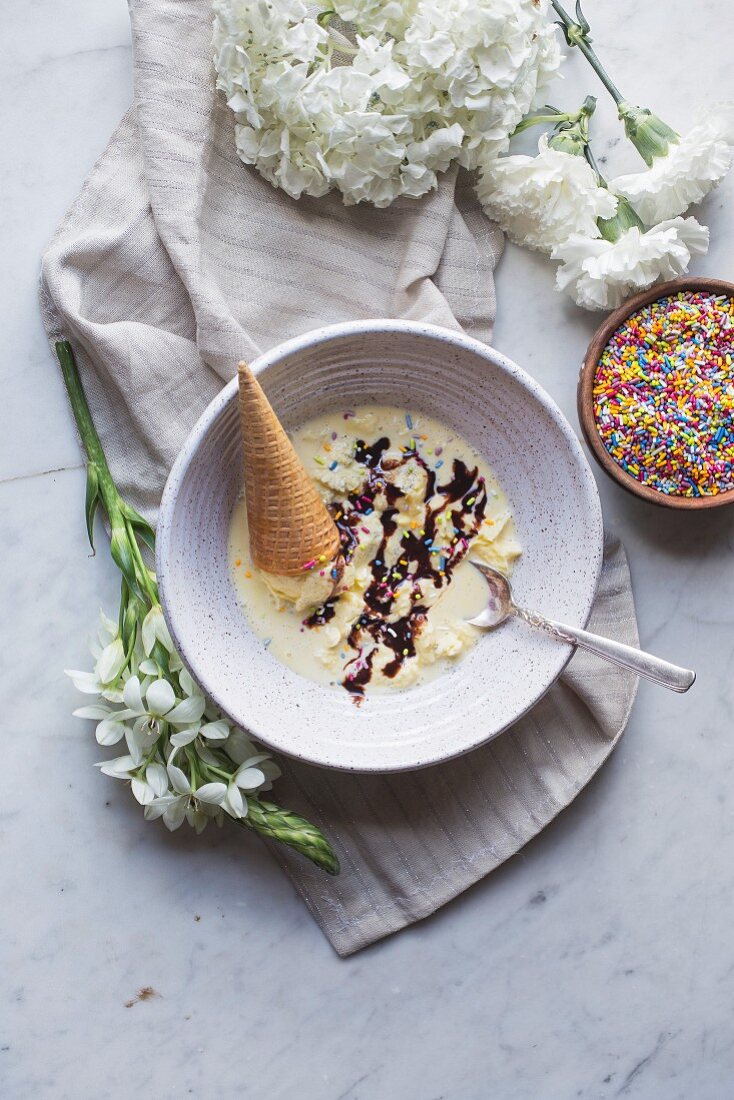 Vanilla ice cream with colourful sprinkles, chocolate sauce and an ice cream cone in a bowl