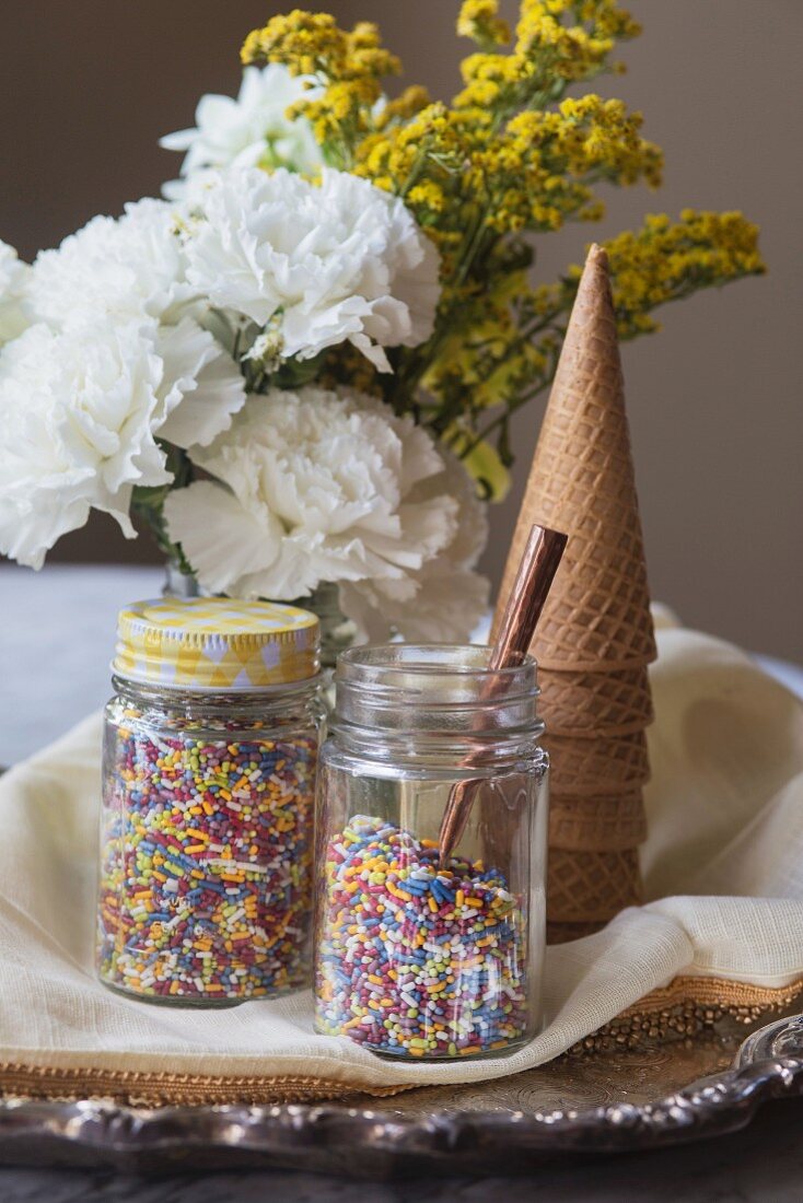 Colourful sprinkles in preserving jars, ice cream cones and flowers