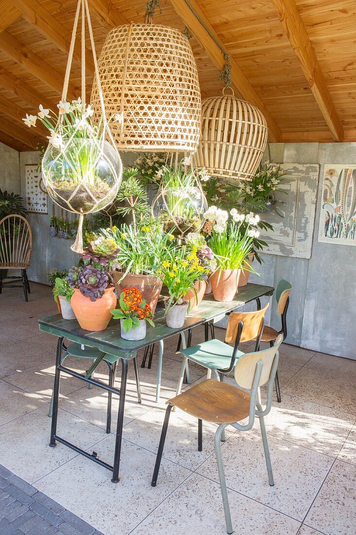 Flowering potted plants on garden table and retro chairs in summer house with three open sides