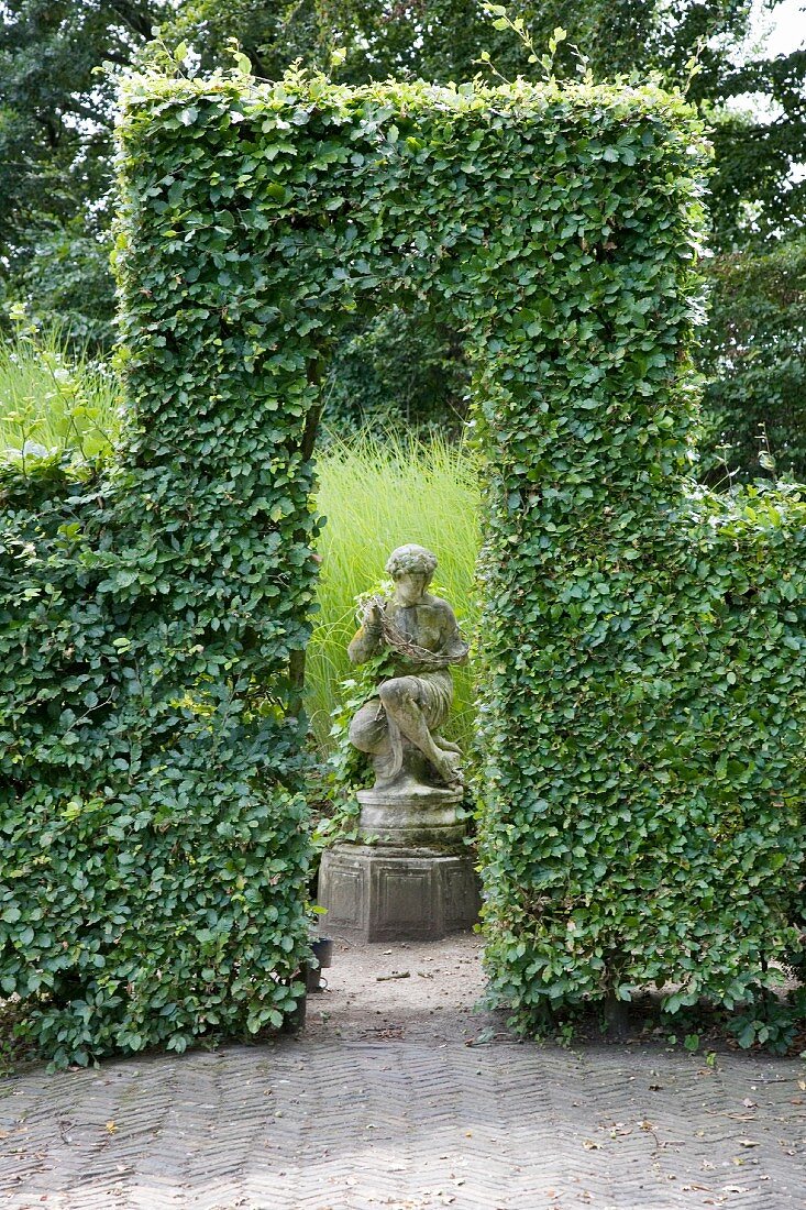 Skulptur hinter dem Durchgang einer Hecke mit Formschnitt