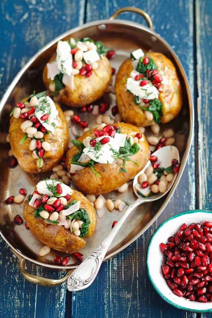 Baked potatoes stuffed with spinach, ham and bean salad and topped with cream cheese and pomegranate seeds