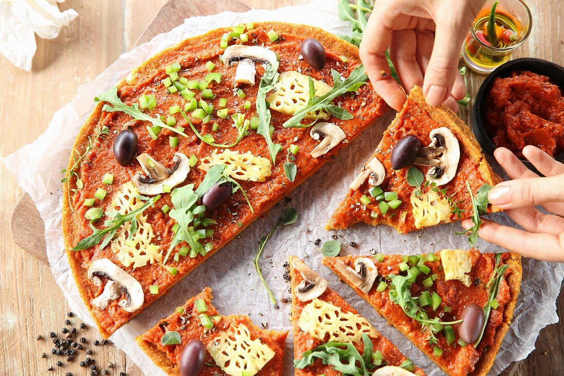 A vegan pizza with pineapple, mushrooms and olives, partly cut into slices