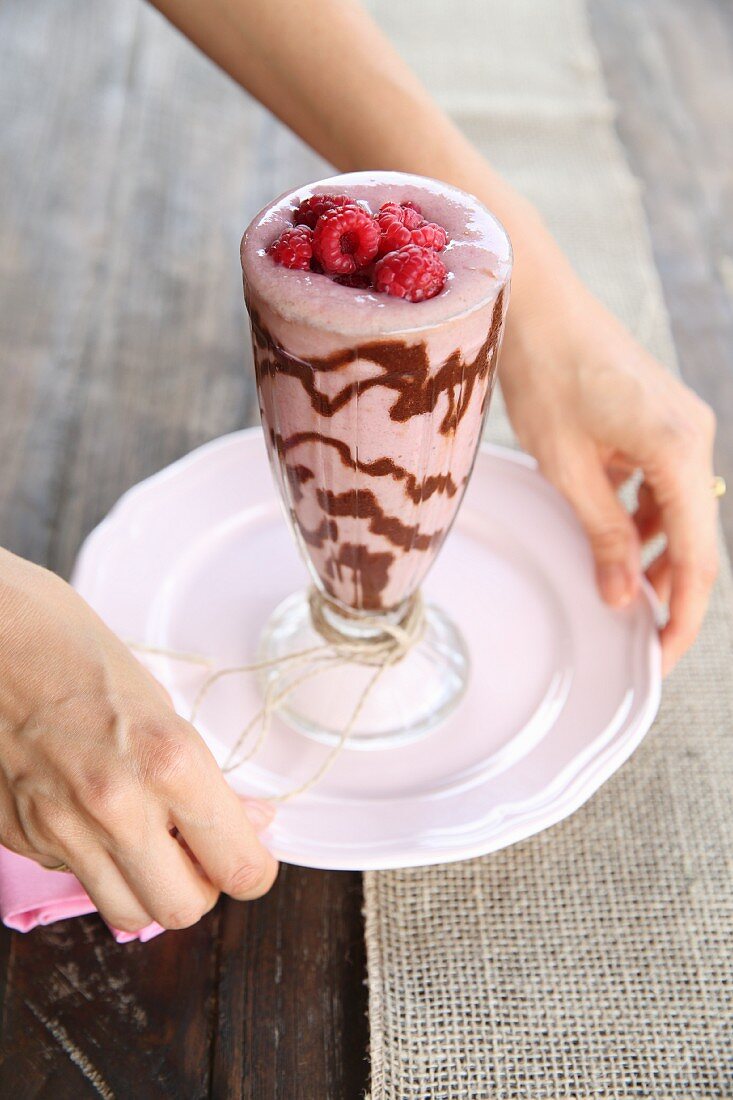 Hands holding a plate with a glass of raspberry and chocolate smoothie