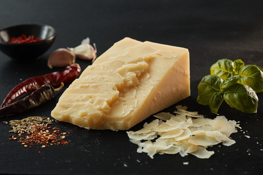 A wedge of Asiago cheese, basil and spices on slate