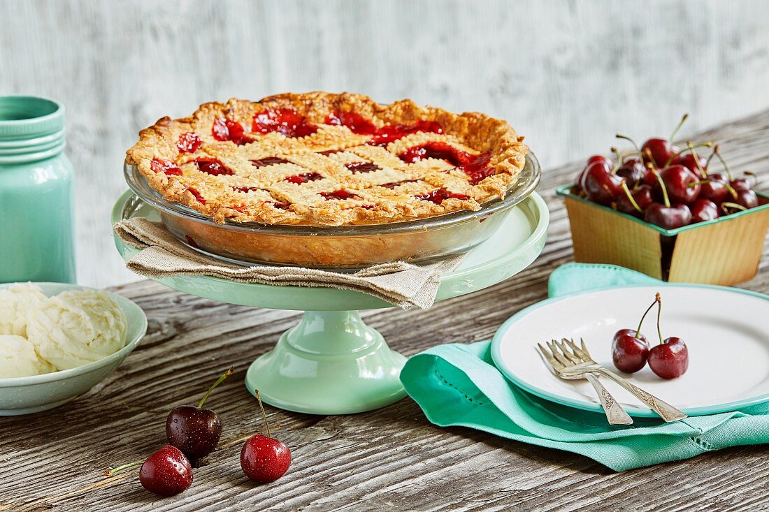 A cherry pie with a lattice top on a cake stand