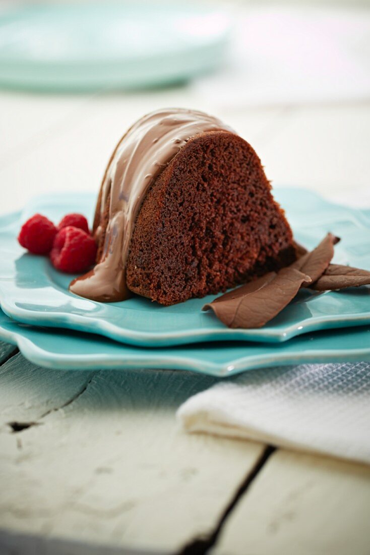A slice of chocolate cake with chocolate icing and raspberries