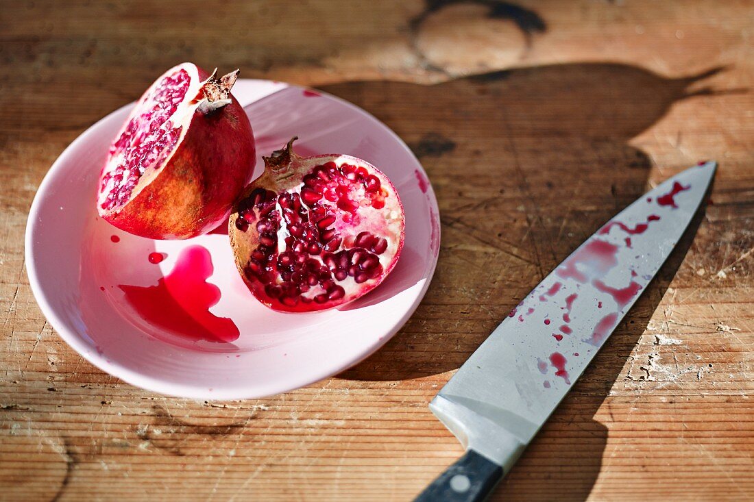 A pomegranate cut in half with a messer on a wooden board