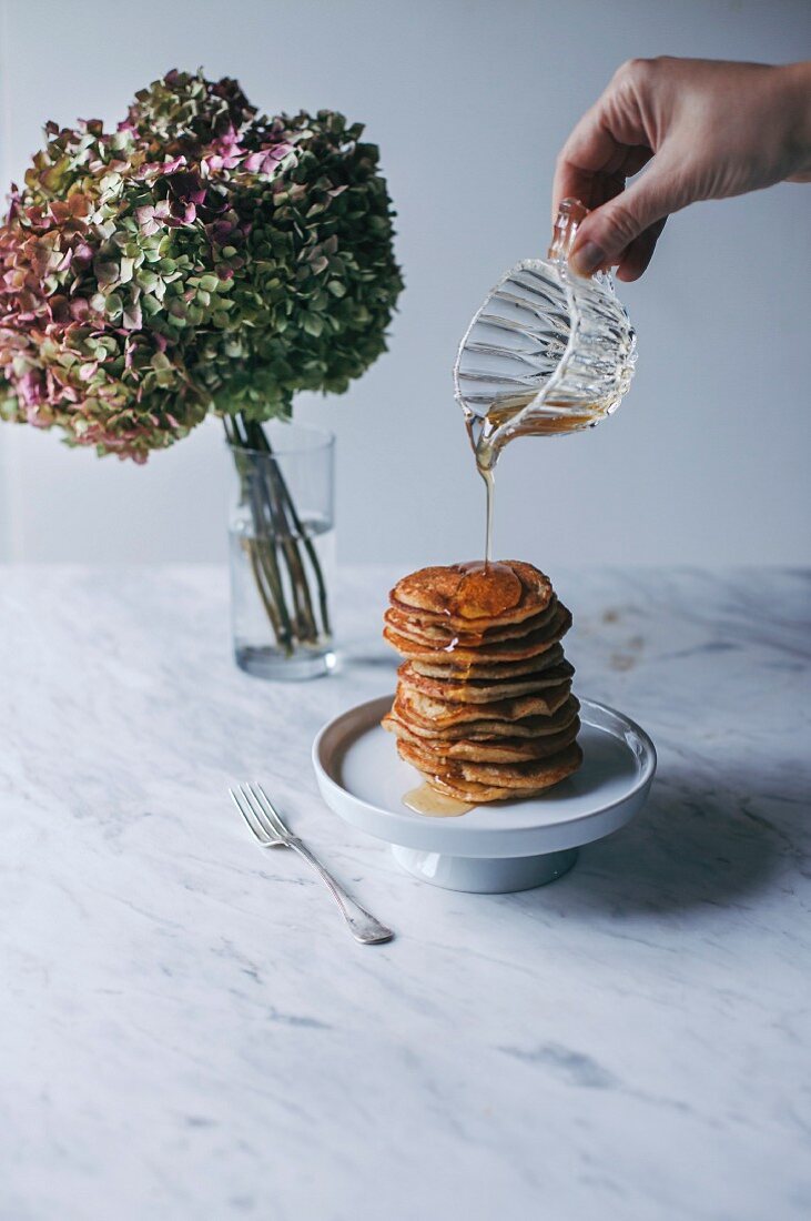 Maple syrup being poured onto a stack of vegan banana pancakes