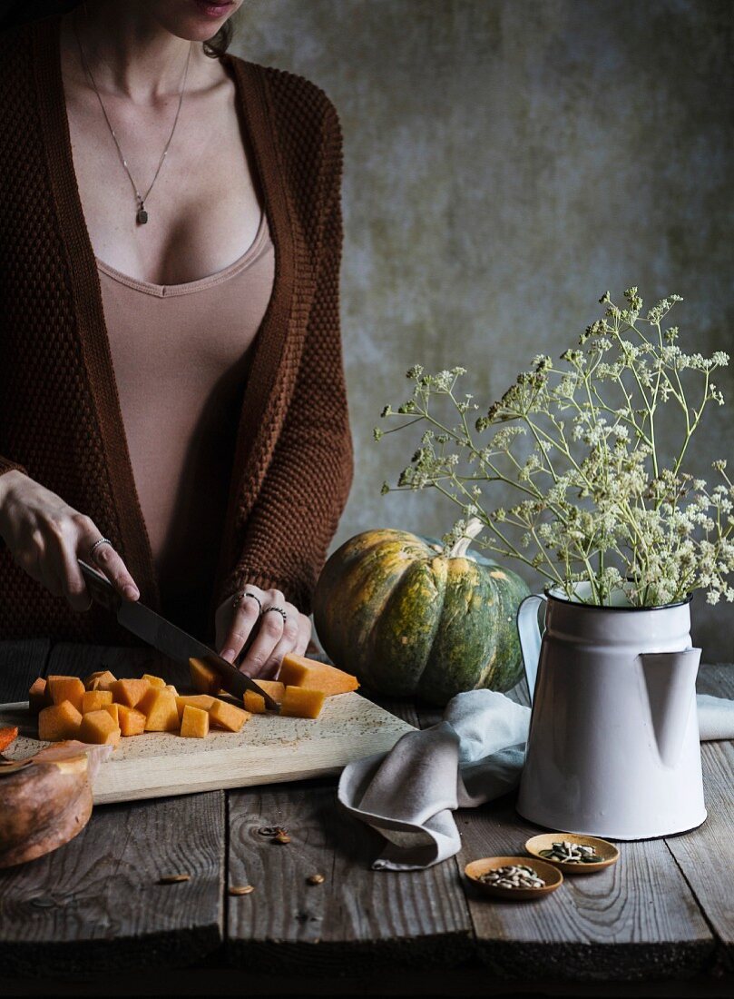 A woman cutting a pumpkin on a rustic wooden table