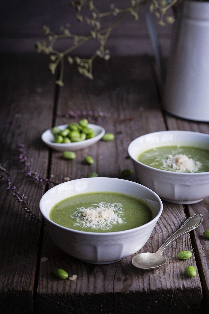 Creamy pea and broad bean with Parmesan in ceramic bowls on a wooden table