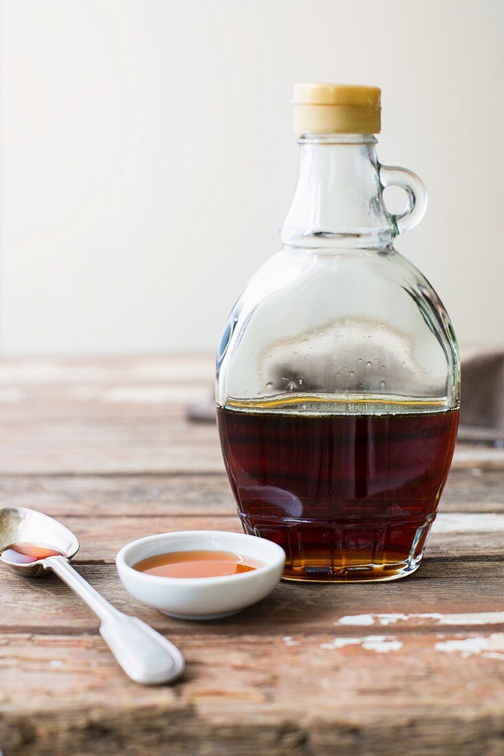 An arrangement of maple syrup in a bottle, in a dish and on a spoon