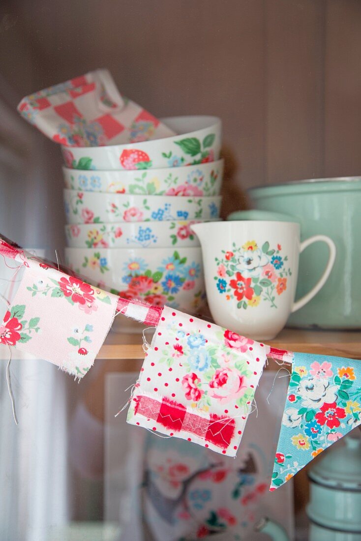 Hand-sewn bunting and floral crockery on shelves of kitchen dresser