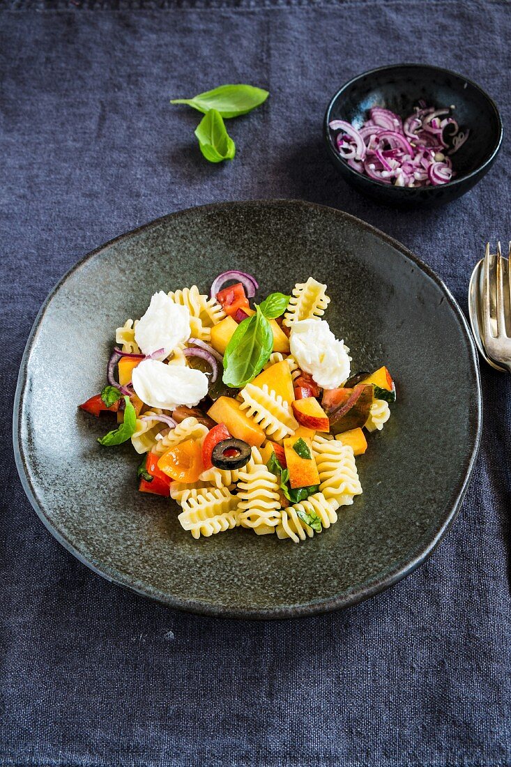 A summery pasta salad with peach, tomatoes and mozzarella