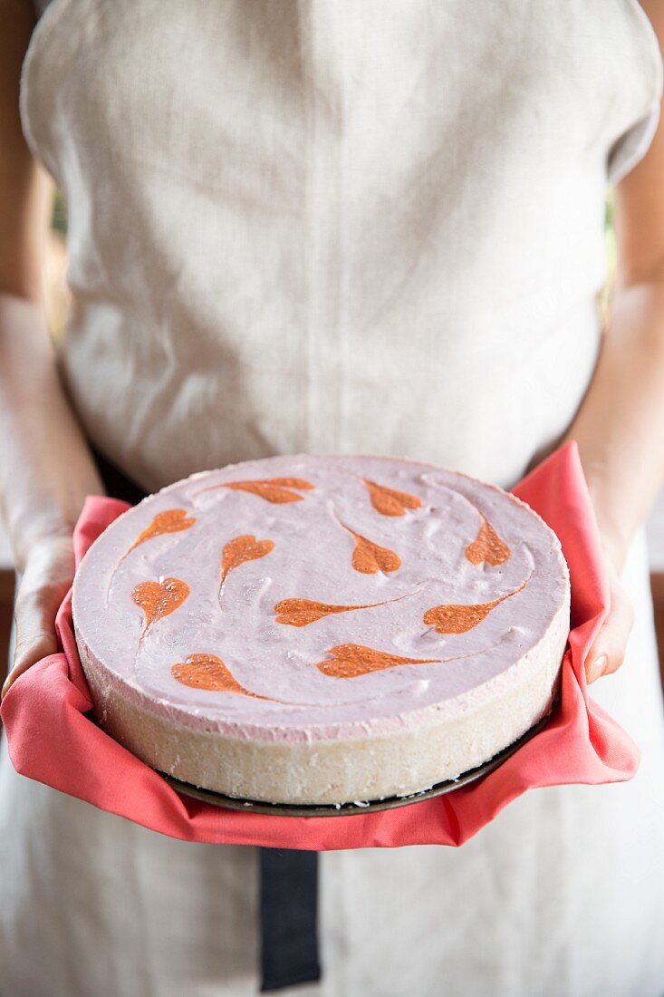 A woman holding a vegan cheesecake with strawberries and goji berries