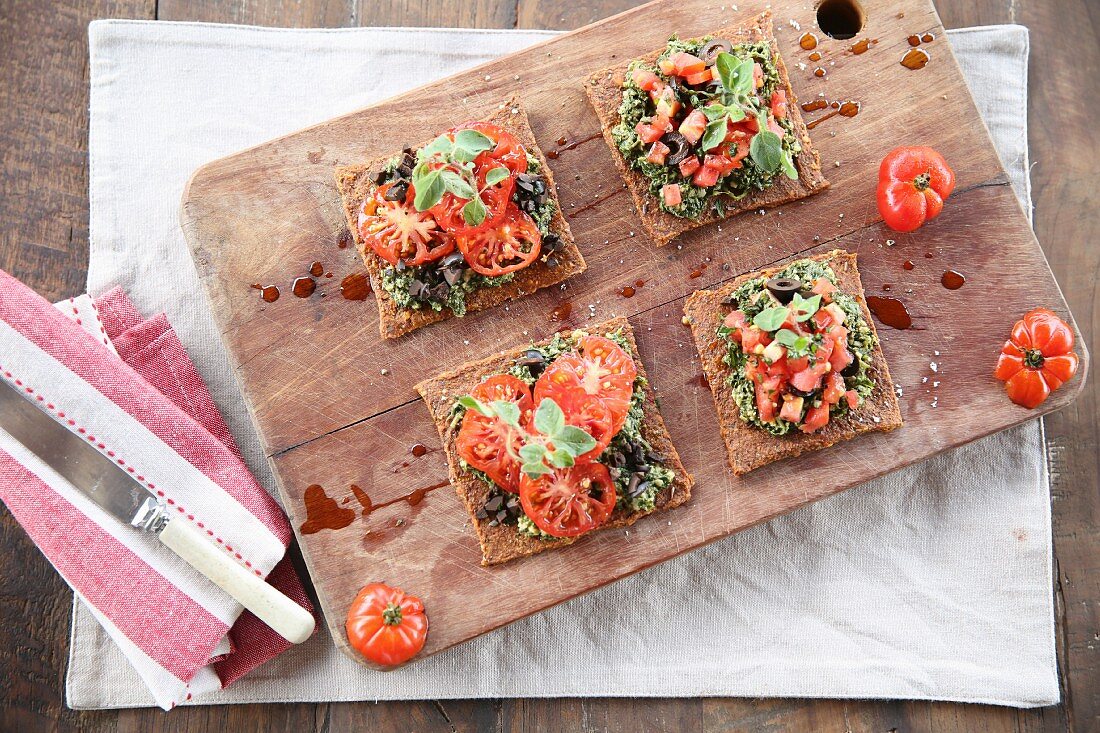 Vegan bruschetta with tomatoes and olives on a wooden board (seen from above)