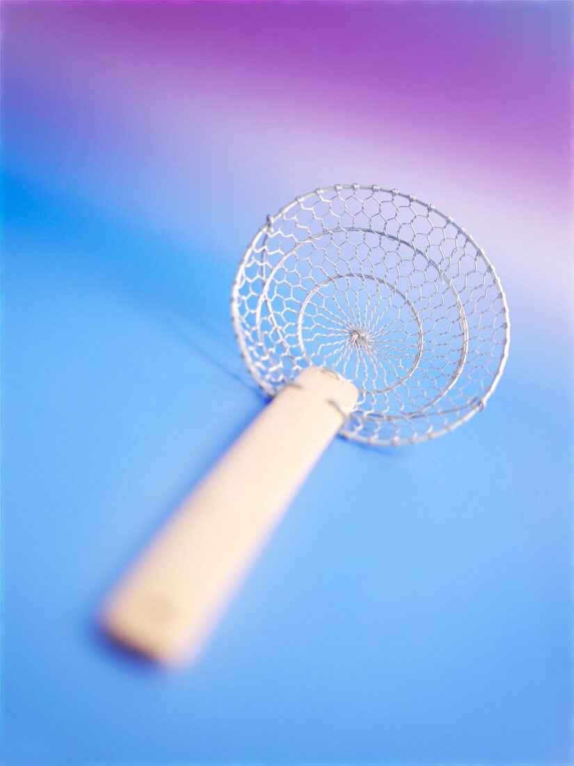 A Chinese fry sieve against a coloured background