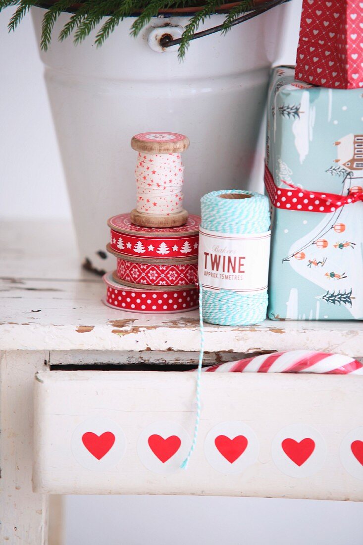 Reels of ribbon and twine and wrapped Christmas gifts on wooden stool with drawer