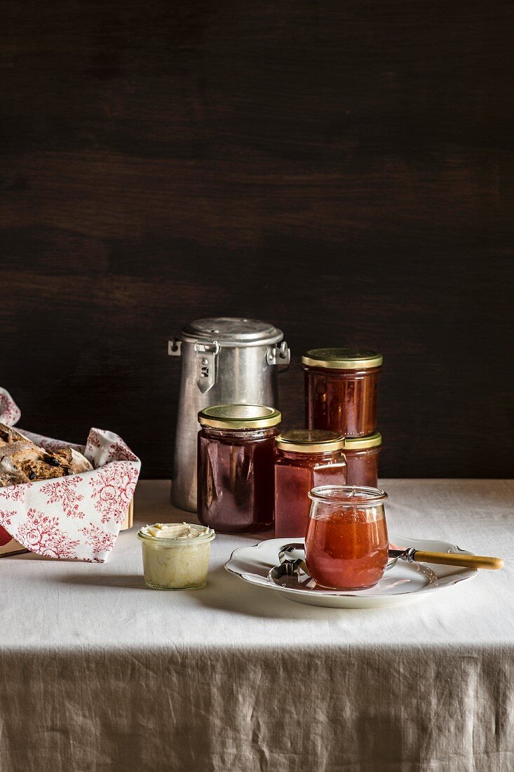 Glass jars with amber colored jam, butter jar and milk can on white table