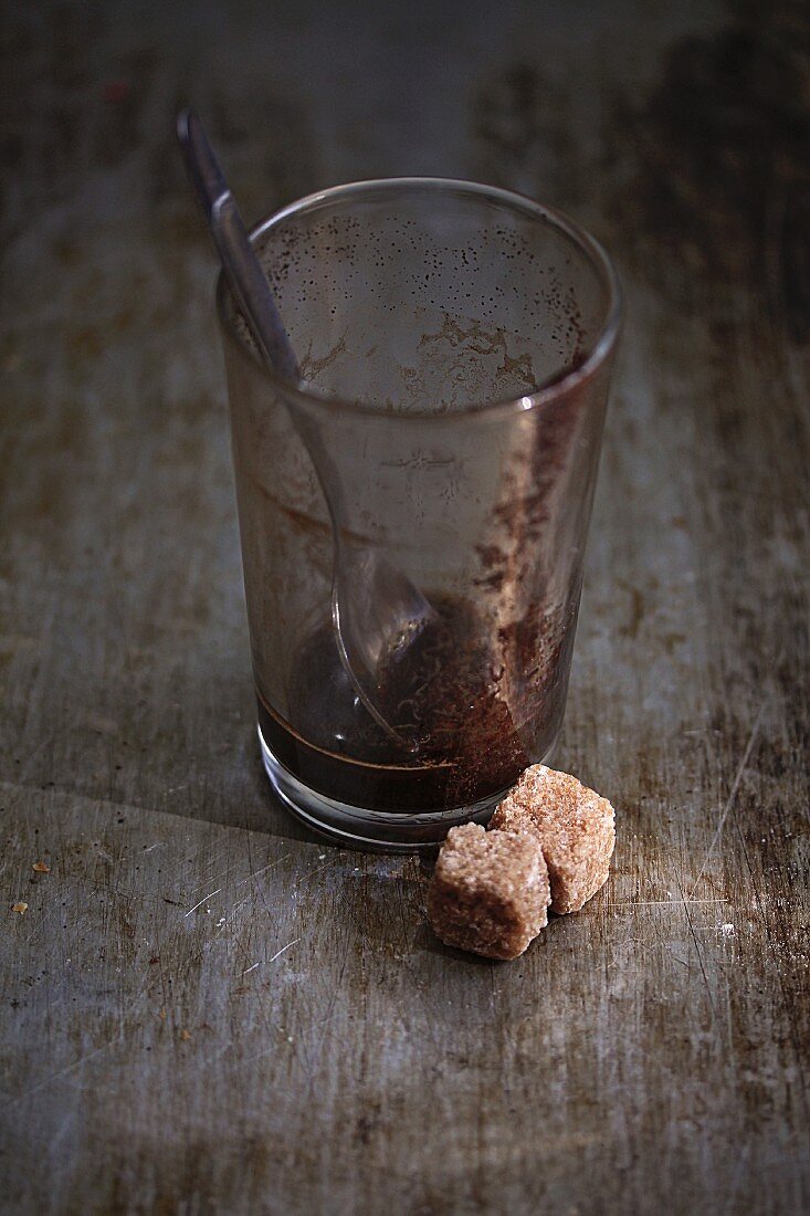 Reste von Kaffee im Glas, davor Rohrzuckerwürfel