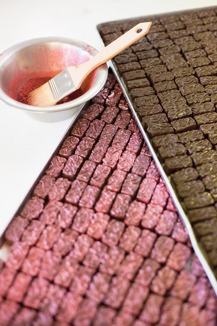 Rows of chocolate pralines, some with pink glazing, on a metal tray