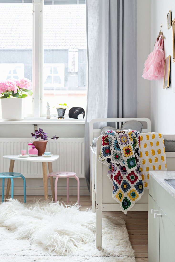 Weisses Kinderbett mit gehäkelter Granny Square-Decke, Kindertisch und Stühle in Mädchenzimmer