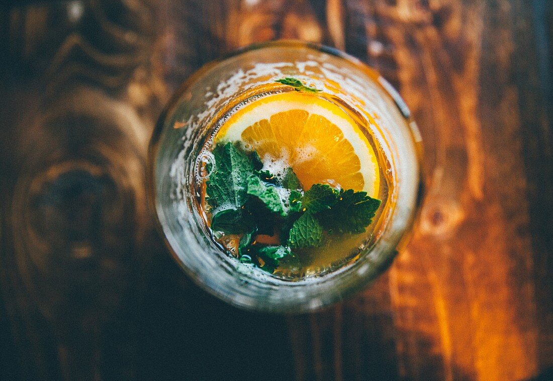A cocktail garnished with a slice of orange and mint