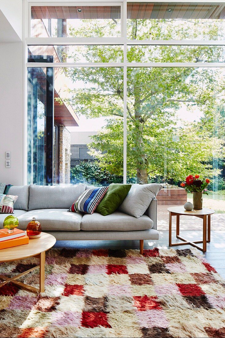 Sofa on colorful carpet in front of panoramic window to garden