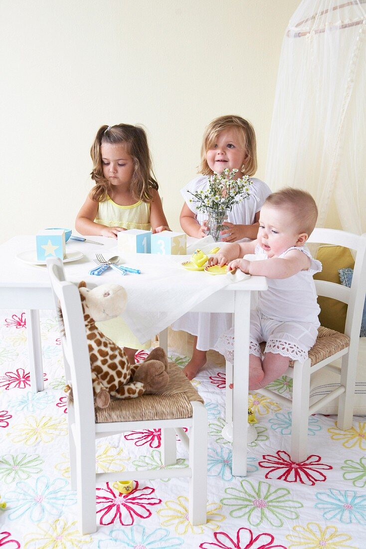 Three toddlers in children's room with white children's table and toys
