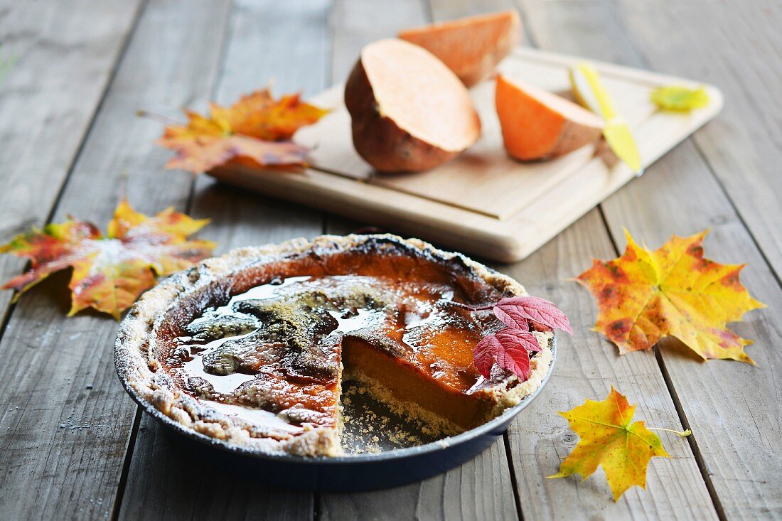 A sweet potato autumn cake decorated with autumn leaves, with a fresh sweet potato in the background