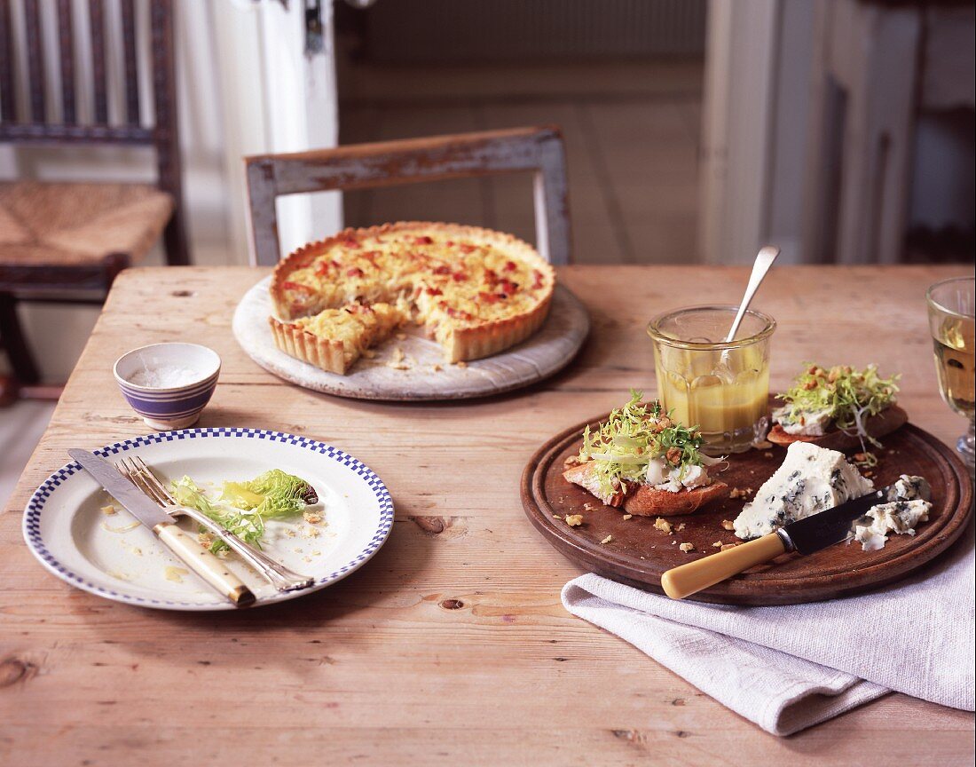 A quiche and slices of baguette topped with blue cheese and salad on a rustic wooden table