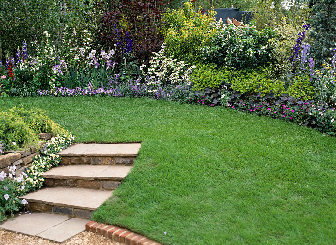 Stairs in the garden with natural stone wall, lawn and flower bed