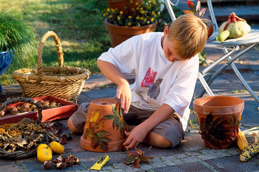 Kind beim Bekleben eines Tontopfes mit buntem Herbstlaub