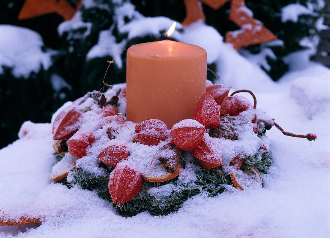 Kranz mit brennender Kerze im Schnee