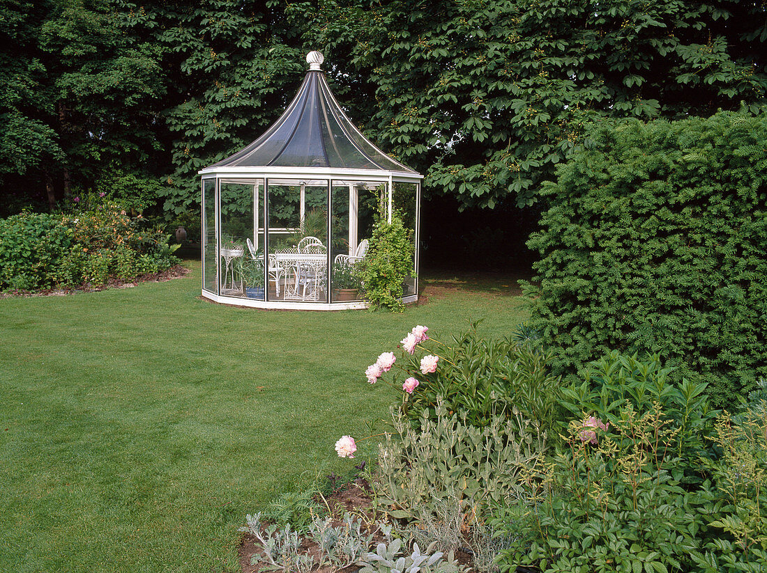 Glass pavilion with white seating in the lawn, Paeonia (peony), Taxus (yew)