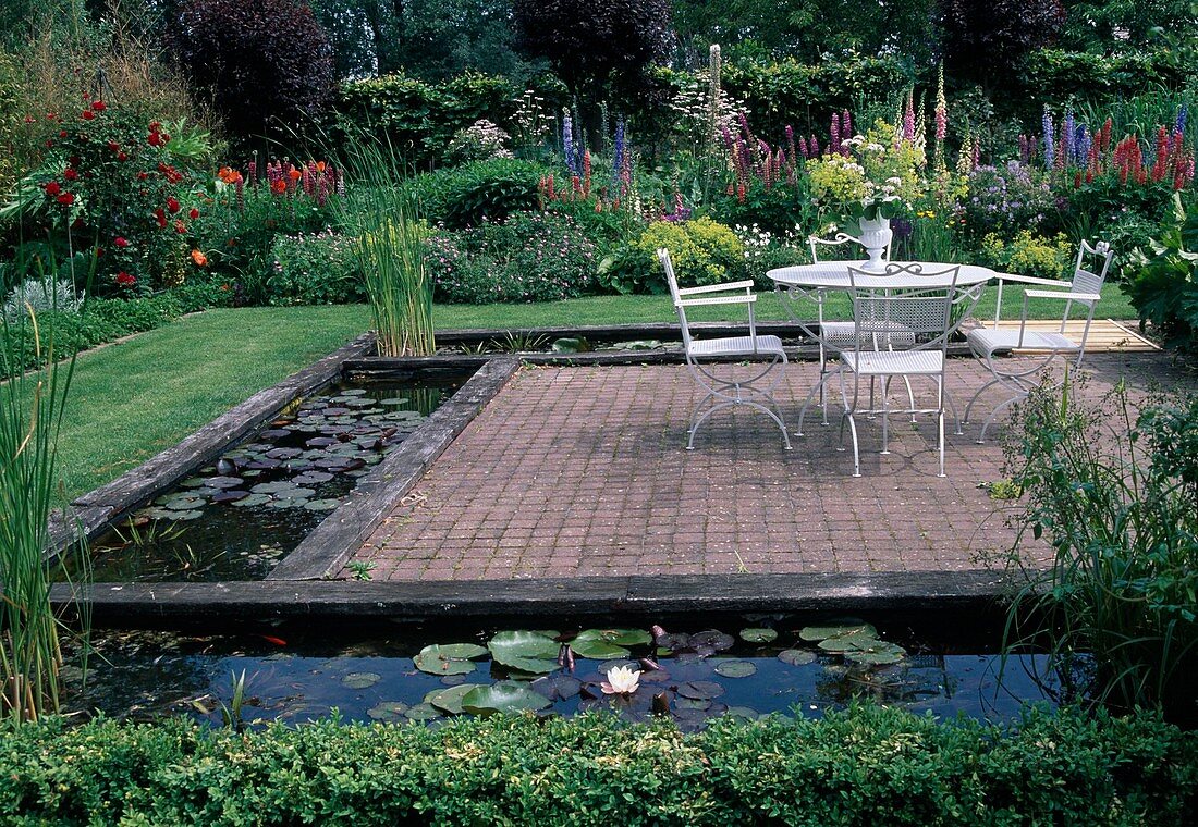 Paved terrace surrounded by rectangular water basins, flowering perennial bed at the back