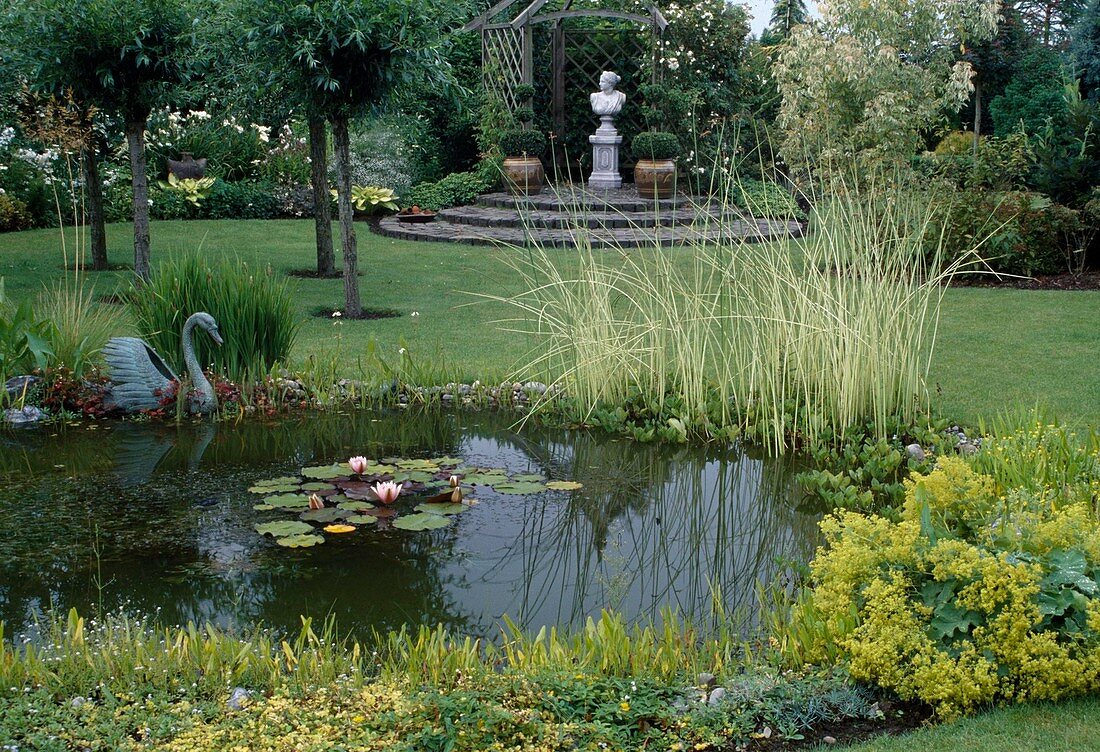 Planted garden pond in large garden, pavilion behind it