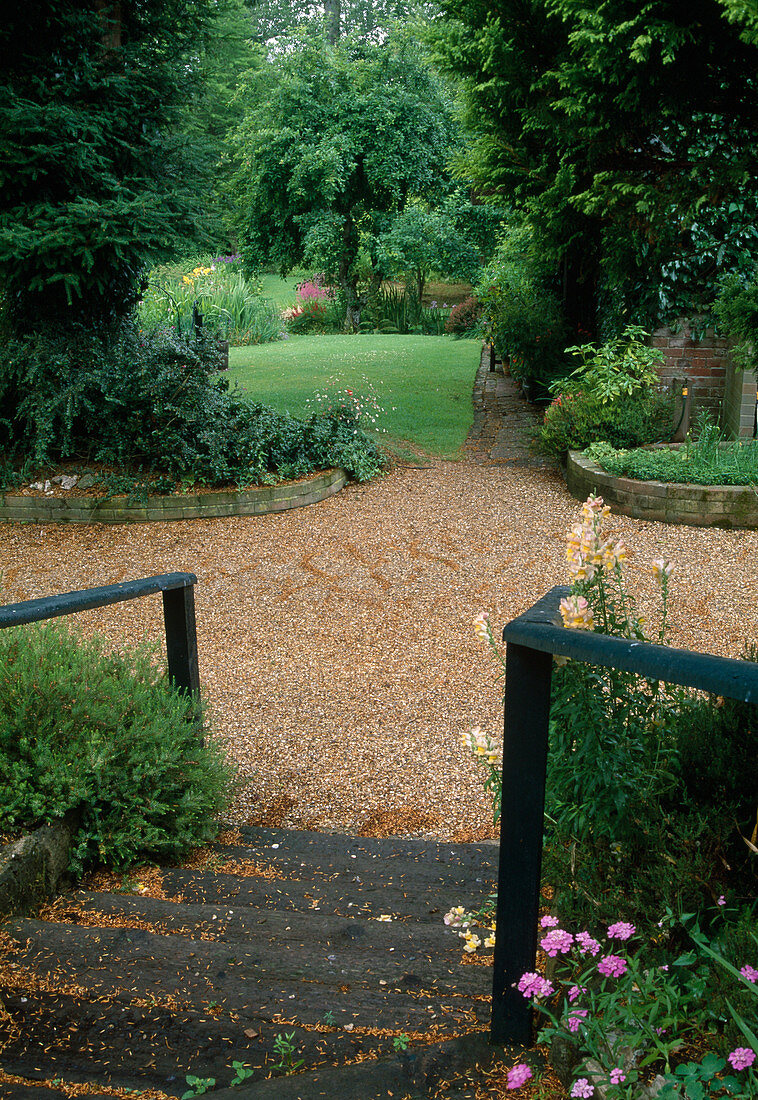 Wooden stairs leading over gravel path into the garden, flower beds bordered with small walls