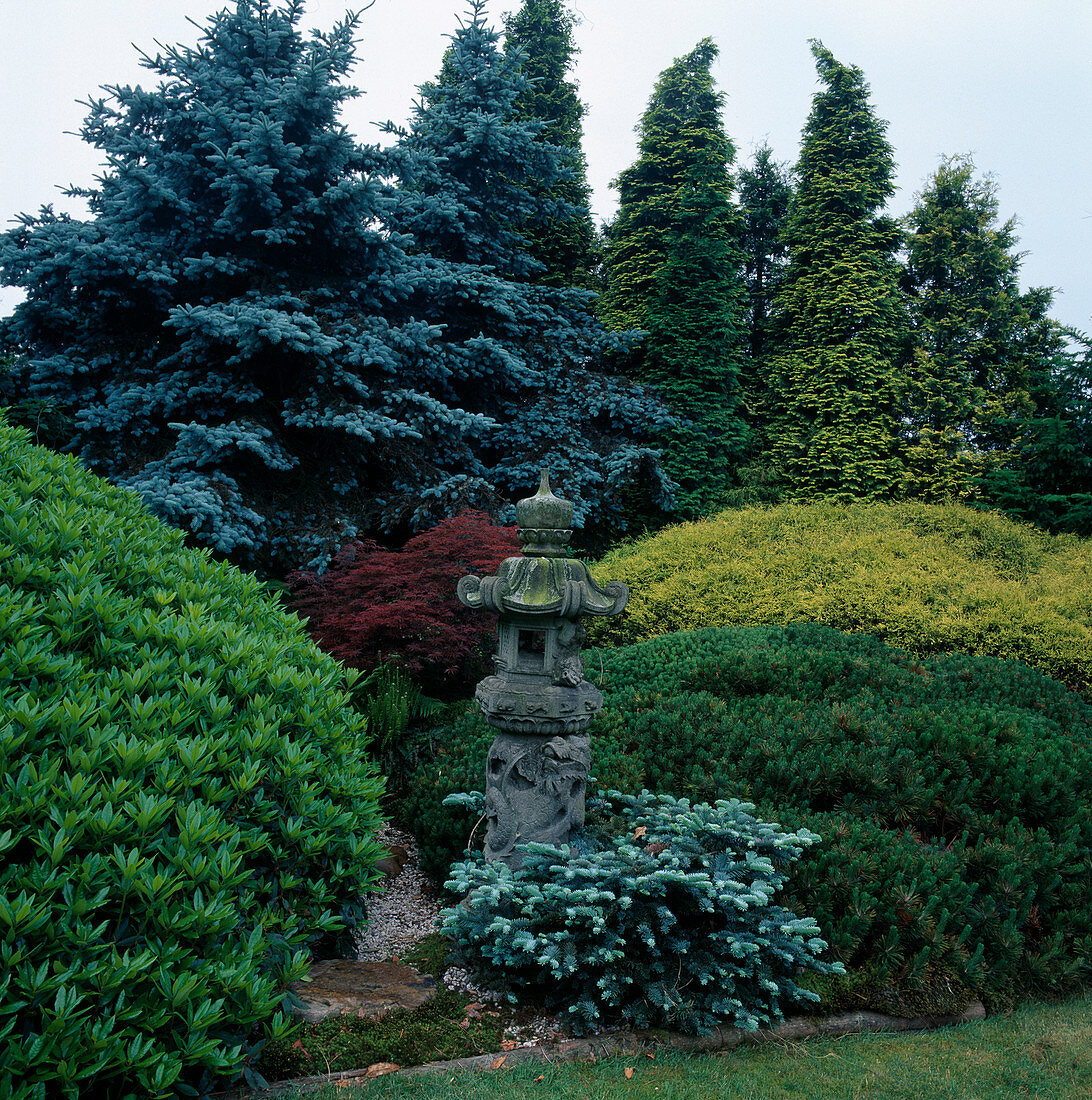 Japanese stone lantern in herbaceous border in front of trees