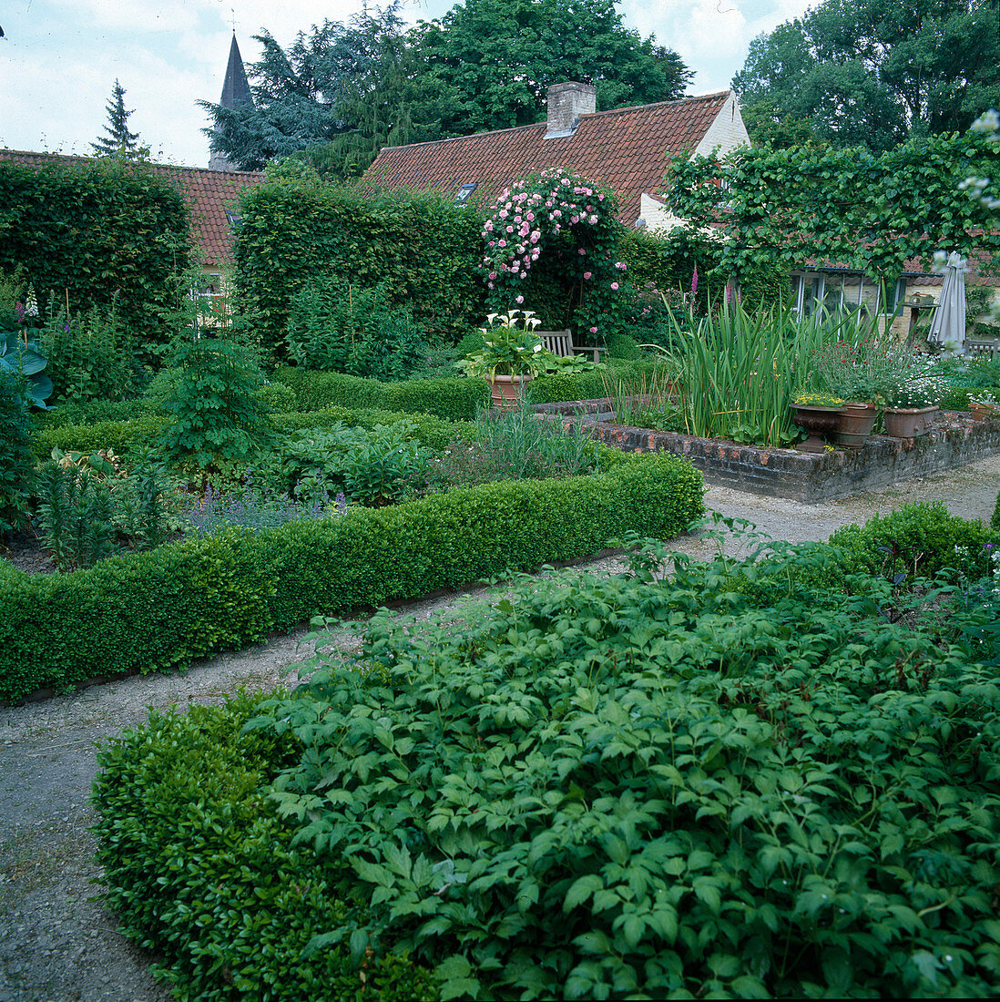 Garten mit niedrigen Buchshecken, Stauden, Rosenspalier und kleinem Teich