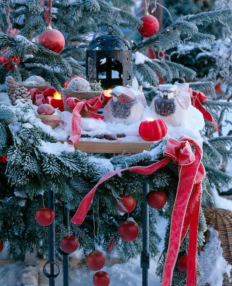 Snow covered table with lantern, candles, fir branches and ribbons