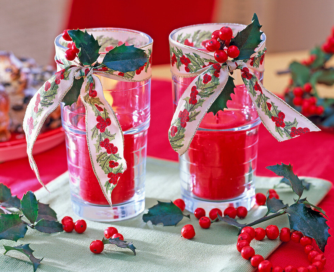 Drinking glasses with red candles, decorated with Ilex (holly, red winterberry)